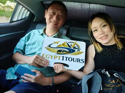 happy tourists holding egypt 1 tours logo banner inside private transfer car from luxor to aswan