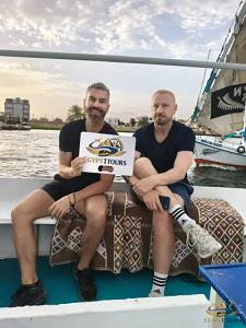 Tourists holding an Egypt 1 Tours sign while relaxing on a private traditional felucca cruise in Luxor