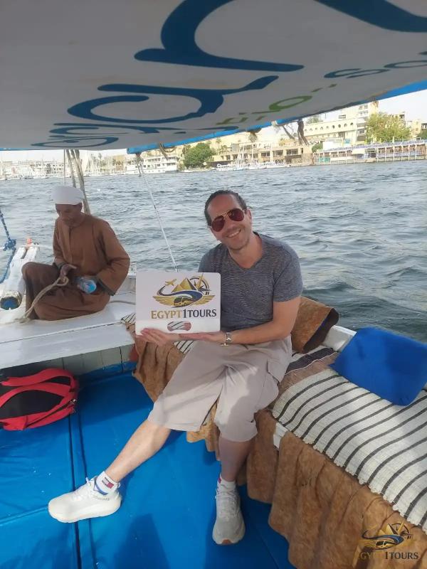 A happy traveler holding an Egypt 1 Tours sign on a private traditional felucca sailing on the Nile in Luxor
