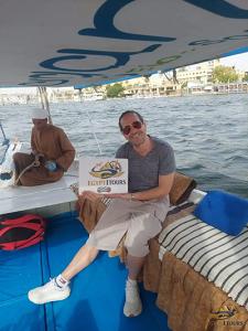A happy traveler holding an Egypt 1 Tours sign on a private traditional felucca sailing on the Nile in Luxor