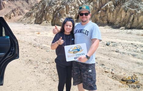 "Happy international clients on the Eastern Desert road from Luxor to Hurghada holding the Egypt1Tours logo sign, proving our private transfer service reliability."