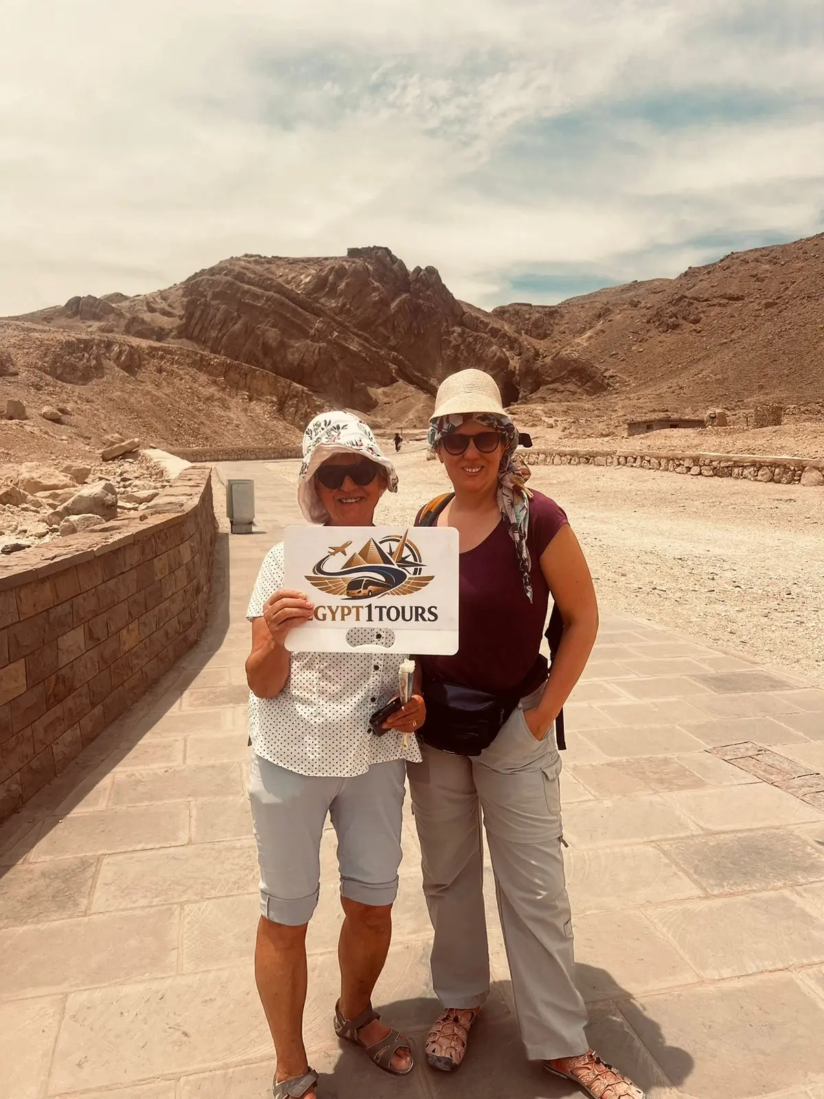 Happy tourists holding Egypt One Tours logo at Valley of the Kings tour.webp